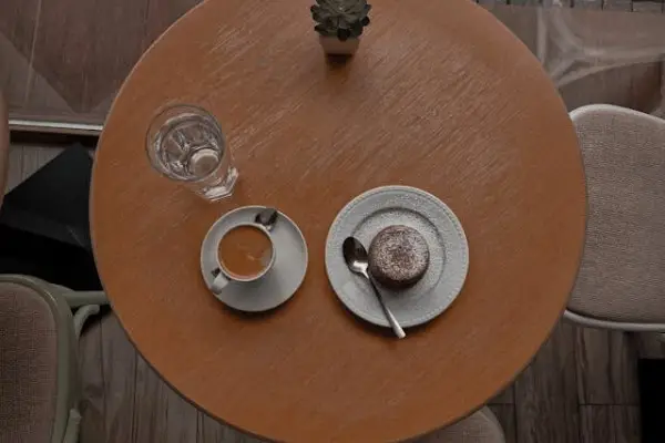 Mesa de madeira de sândalo vista de ângulo superior, arrumada para um café com bolo individual