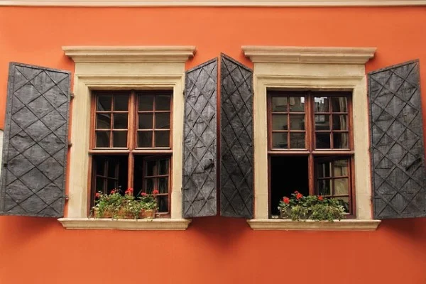 Janelas de madeira verticais usadas reaproveitadas, com vaso de flor e parede laranja